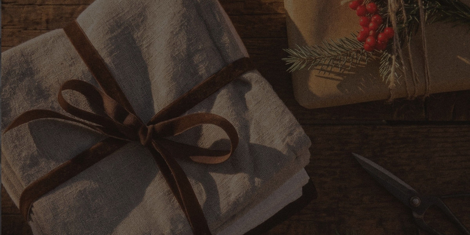 Natural linen gift tied with brown ribbon beside holly and wrapping