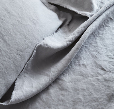 closeup detail of 100% linen summer cover blanket with frayed raw edge detail light grey color